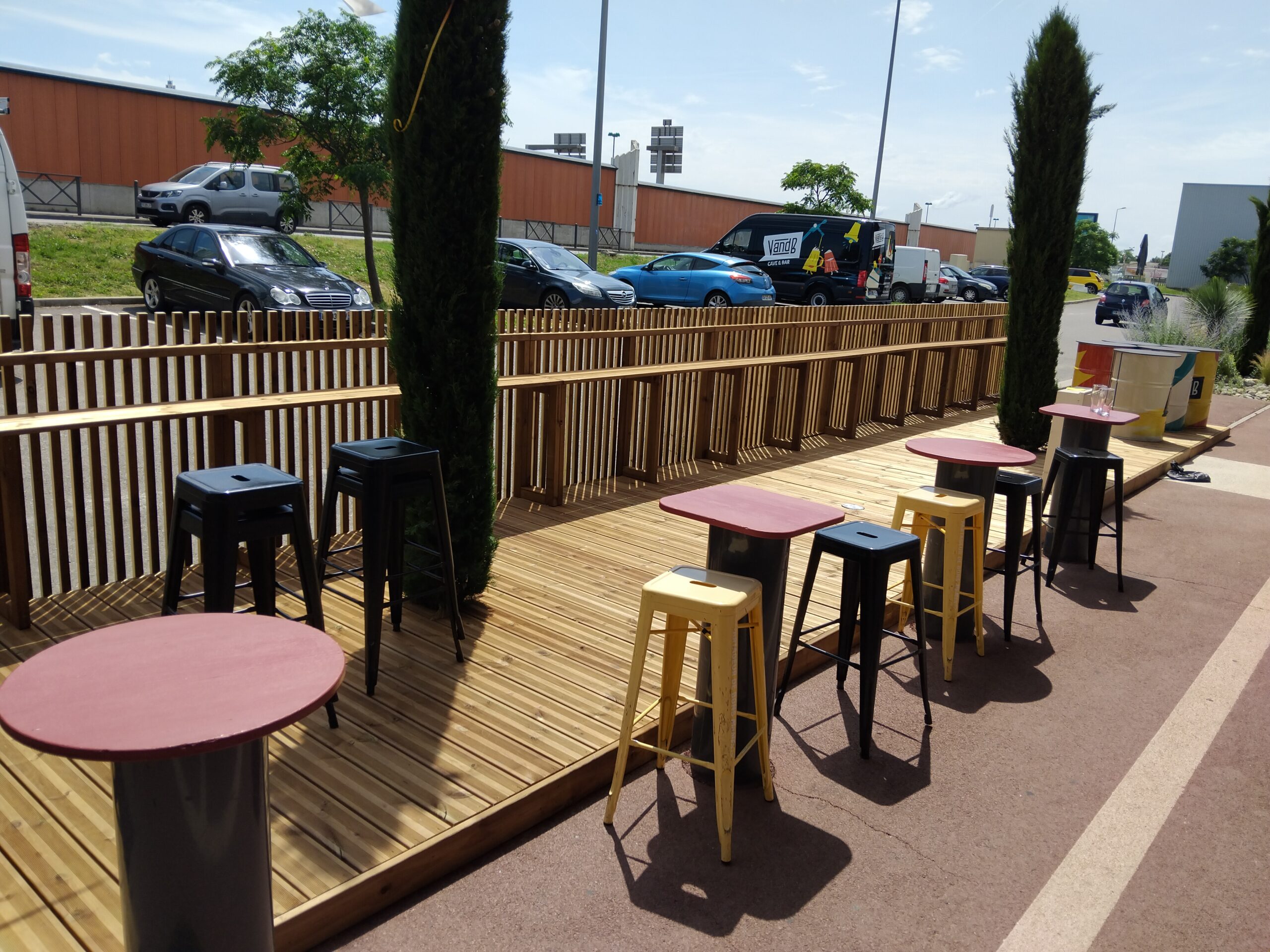 Terrasse bois moderne avec tables rouges et tabourets chez dr-menuiserie, aménagement extérieur chaleureux dans le Tarn