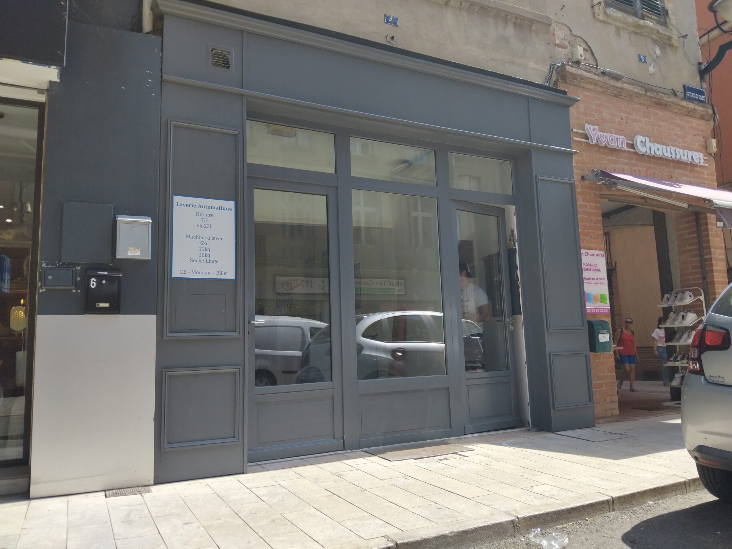 Rue commerçante ensoleillée à Tarn avec laverie, magasin Yuan Chaussures et vitrine dr-menuiserie